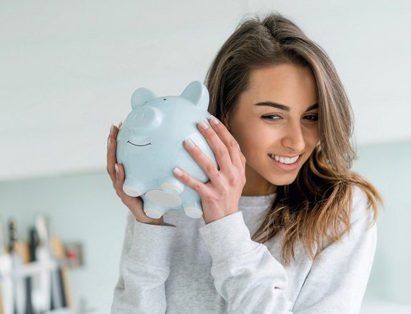 Junge Frau mit Sparschein in den Händen, ans Ohr haltend