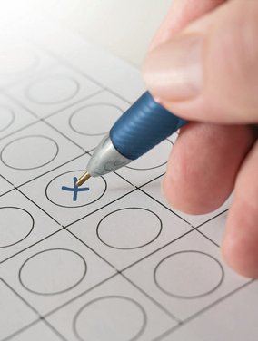 Hand mit Kugelschreiber kreuzt einen Wahlzettel an