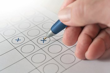 Hand mit Kugelschreiber kreuzt einen Wahlzettel an