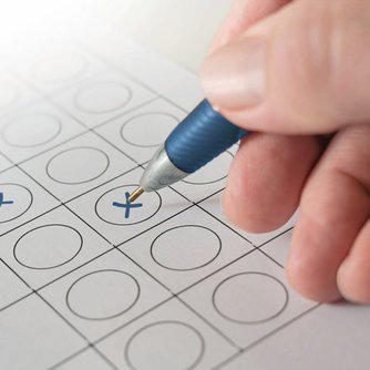 Hand mit Kugelschreiber kreuzt einen Wahlzettel an