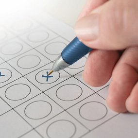 Hand mit Kugelschreiber kreuzt einen Wahlzettel an