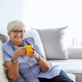 Ältere Frau mit gleber Tasse in der Hand auf dem Sofa sitzend